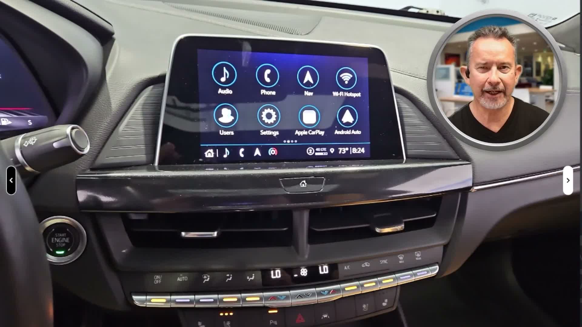 Video frame: a car's dashboard touchscreen fills the screen while the salesperson talks from a small circle camera in the top corner.